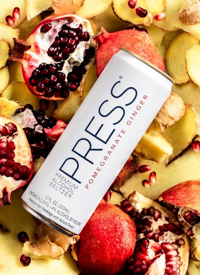 Can of Press hard seltzer on a bed of sliced ginger and opened pomegranates, remote product photography