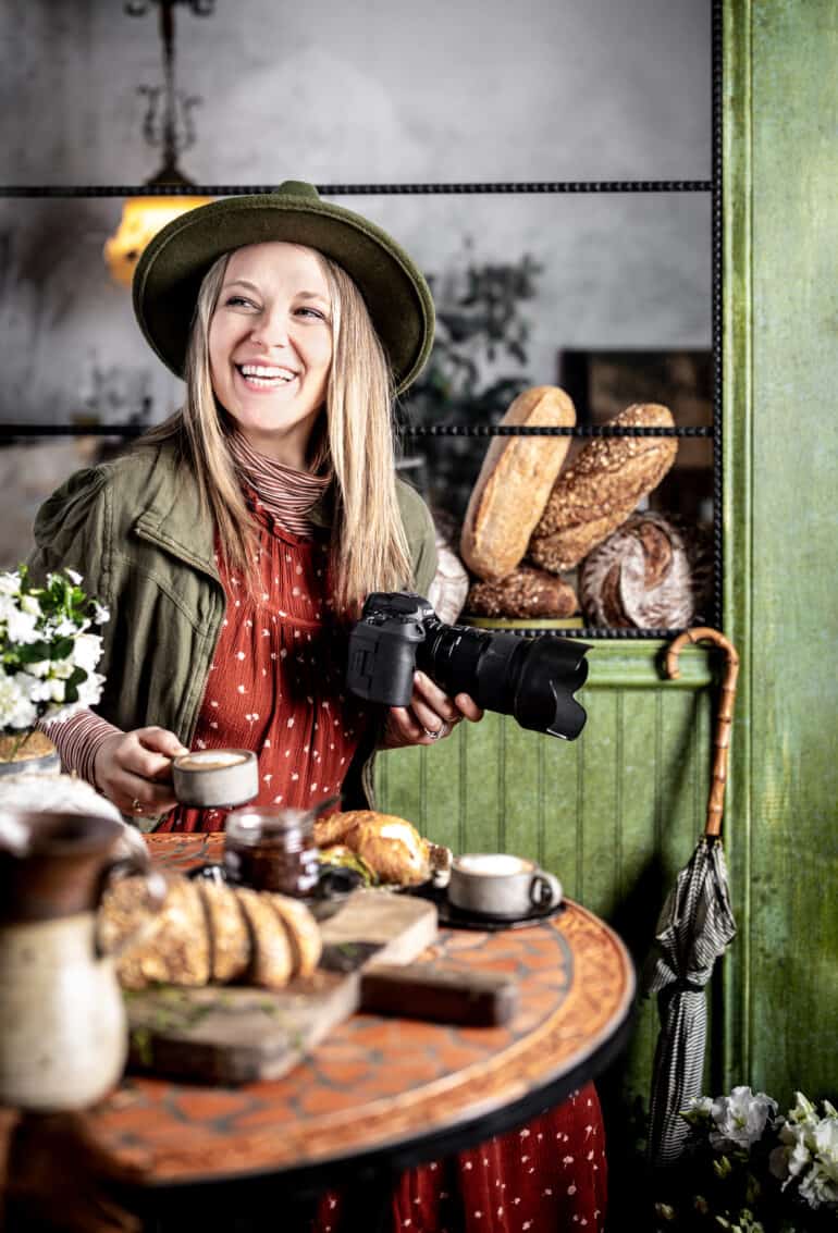 Jena Carlin sitting in a bakery set in her studio with camera  and coffee