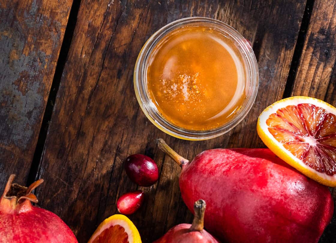 A beautiful golden vinaigrette in a glass jar with vibrant red fruits