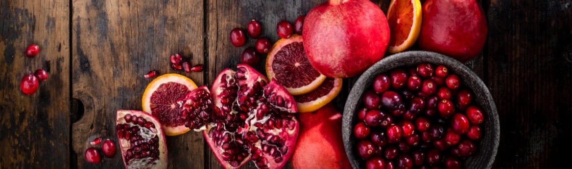 Artful spray of vibrant red winter fruits on a rustic table. Pomegranate, cranberries, blood oranges, red pears