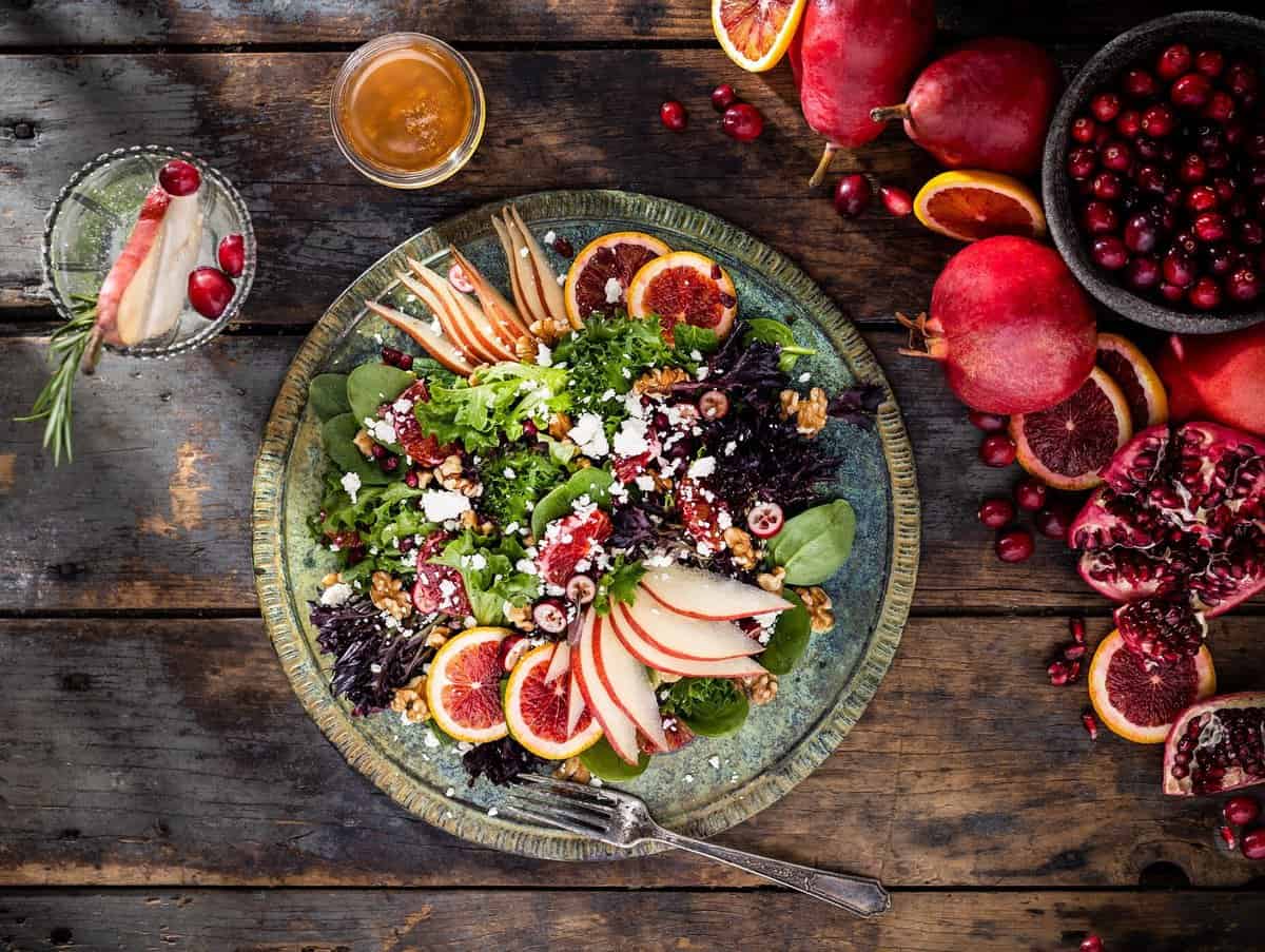 Large plated winter fruits salad with blood orange, red pear, cranberry, pomegranate, feta cheese, and walnuts. Served with vinaigrette and pear fizz cocktail  