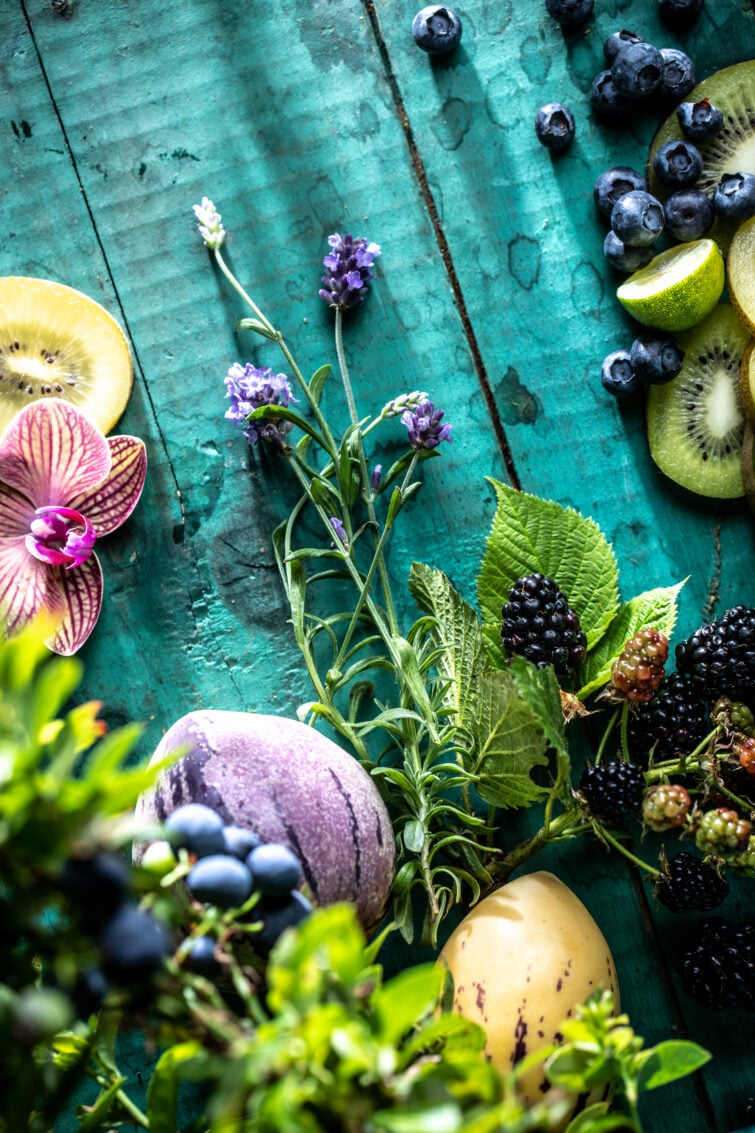 Overhead fruit flood of tropical fruits and flowers on a bright teal wooden food background 