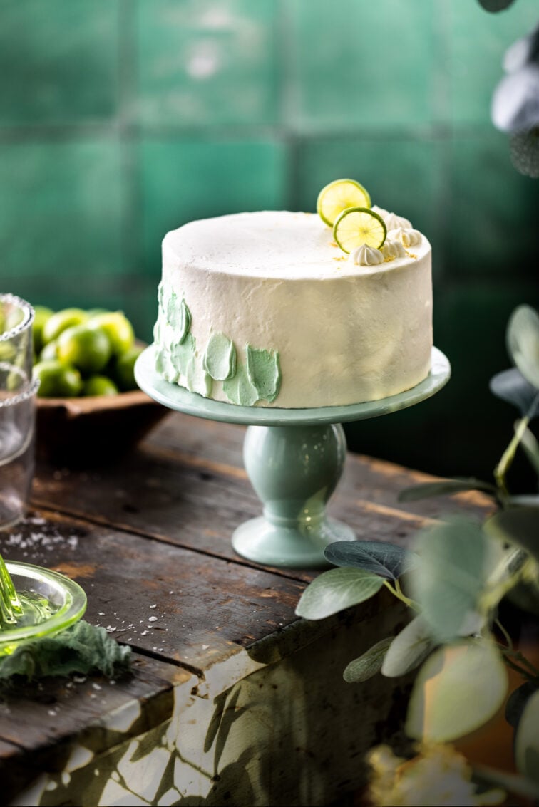 A key lime cake on a eggshell blue stand with a printed tile background in the distance