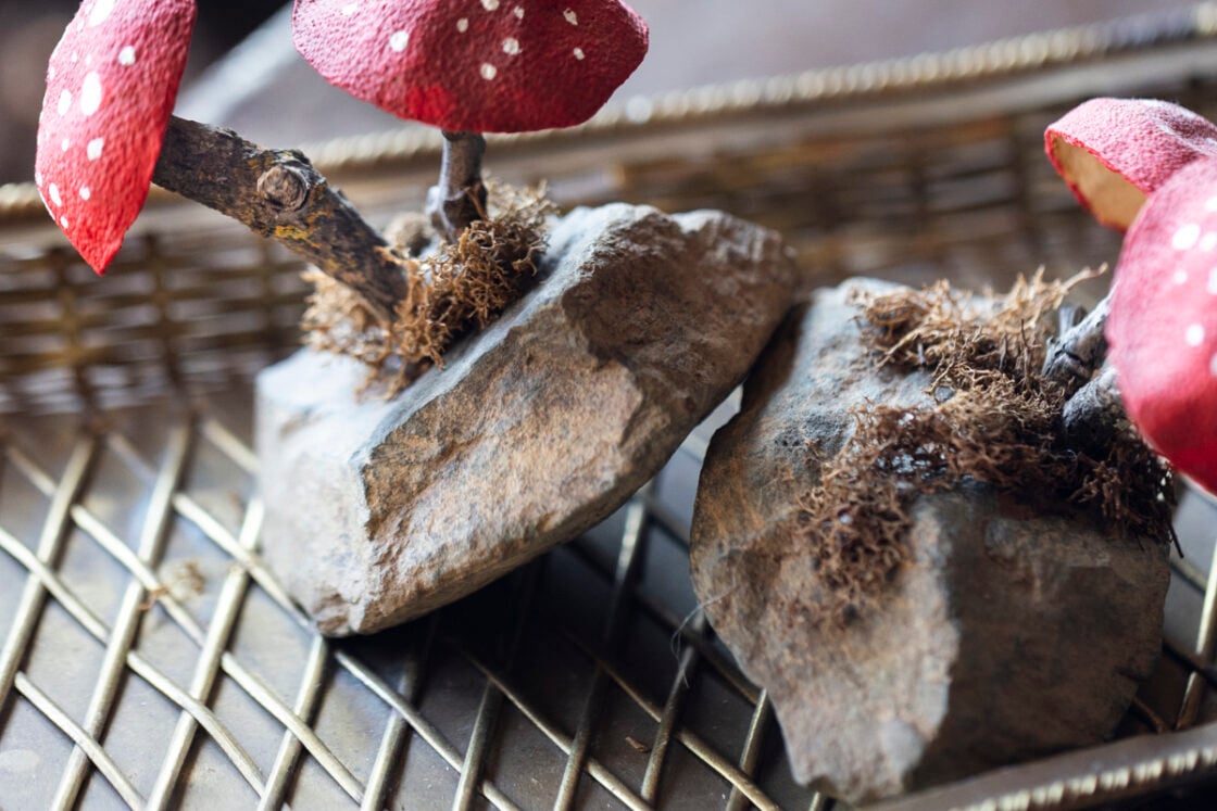 detail close up of moss, stick and mushroom glued onto a small flat rock