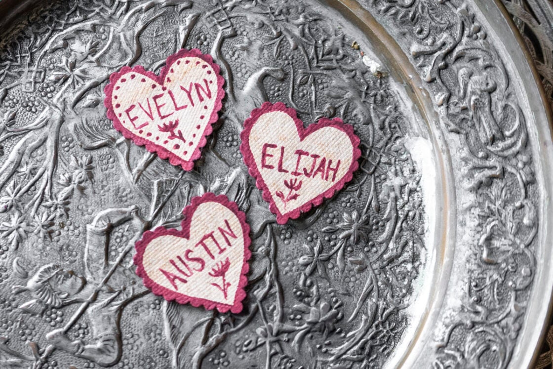 Hand-painted vintage paper heart name tags on DIY mushroom decor photographed overhead on textured metal plate
