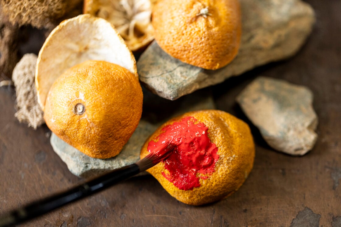 Curved dried orange peel shaped into mushroom cap being painted red for tablescape decoration